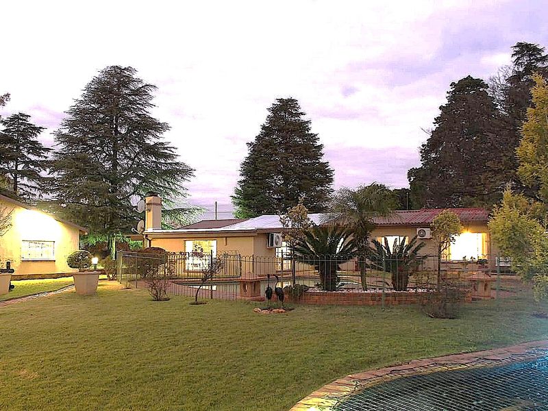 A view of the rear garden featuring a swimming pool, landscaped lawn, and the rear elevation of the farm-style residence at dusk.