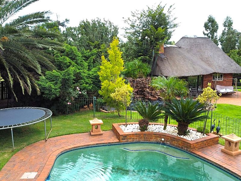 A well-maintained outdoor pool area featuring brick paving, a stone water feature, and a charming thatched-roof structure set within a lush garden.
