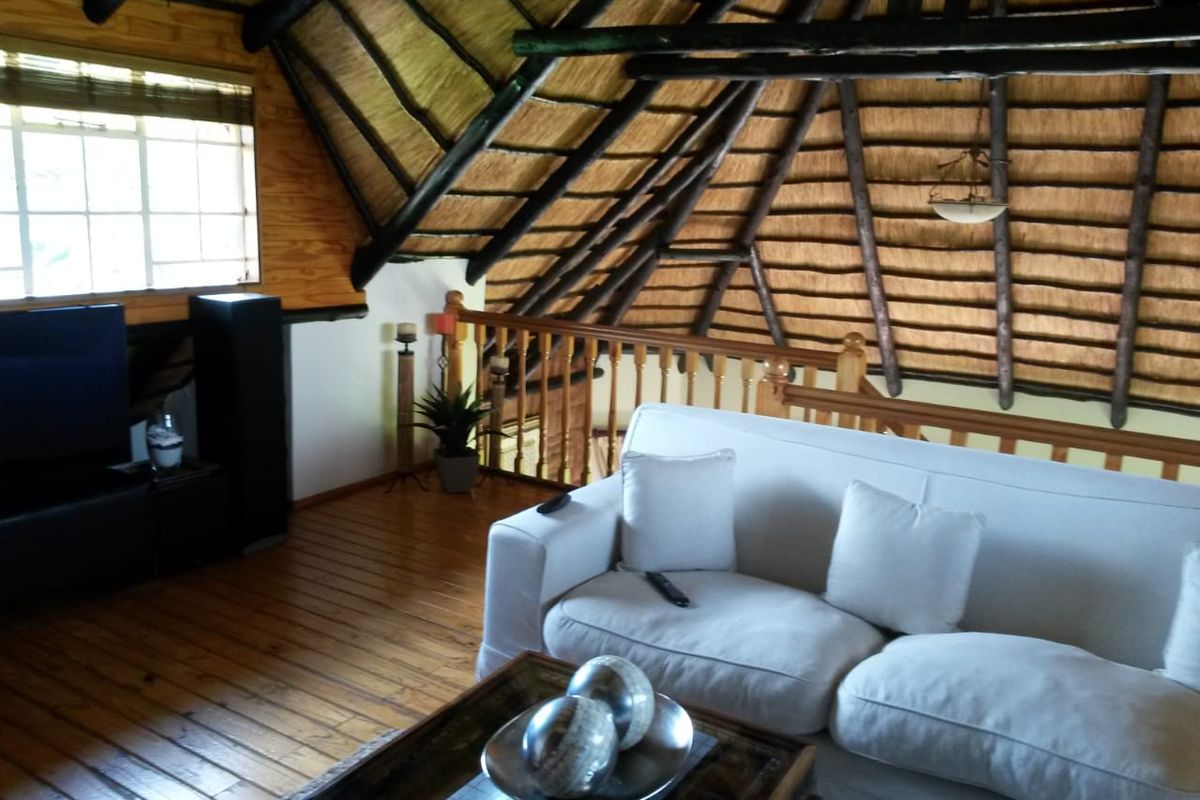 A cozy loft-style living area featuring a traditional thatched roof with exposed timber rafters, wooden flooring, and a timber balustrade overlooking the lower level.
