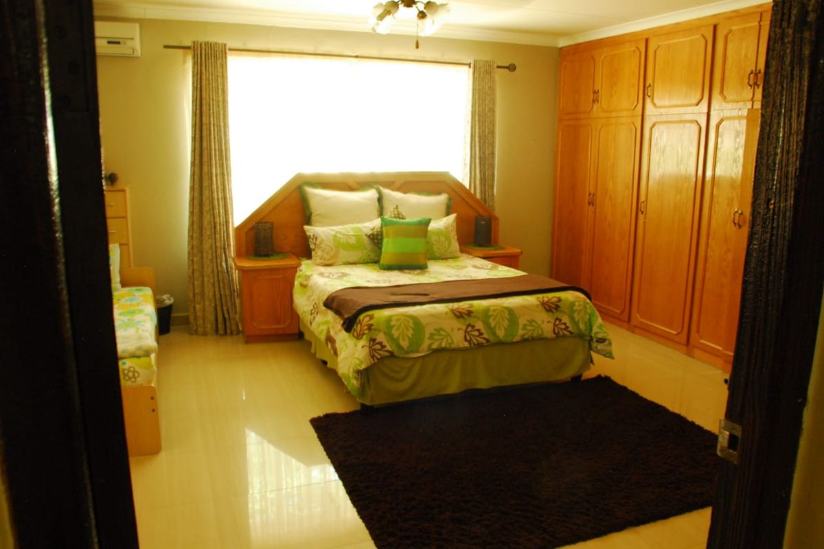 Spacious bedroom featuring built-in wooden cupboards, tiled flooring, and an integrated air conditioning unit.