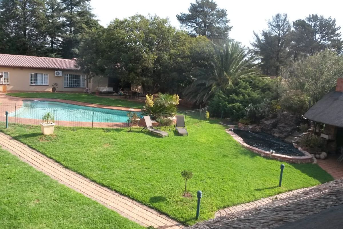 Spacious rear garden featuring a swimming pool with safety fencing, a paved walkway, and a charming thatched-roof outdoor area set within a landscaped yard.