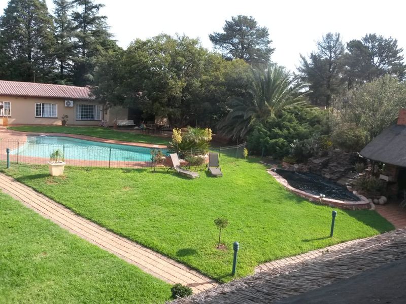 Spacious rear garden featuring a swimming pool with safety fencing, a paved walkway, and a charming thatched-roof outdoor area set within a landscaped yard.