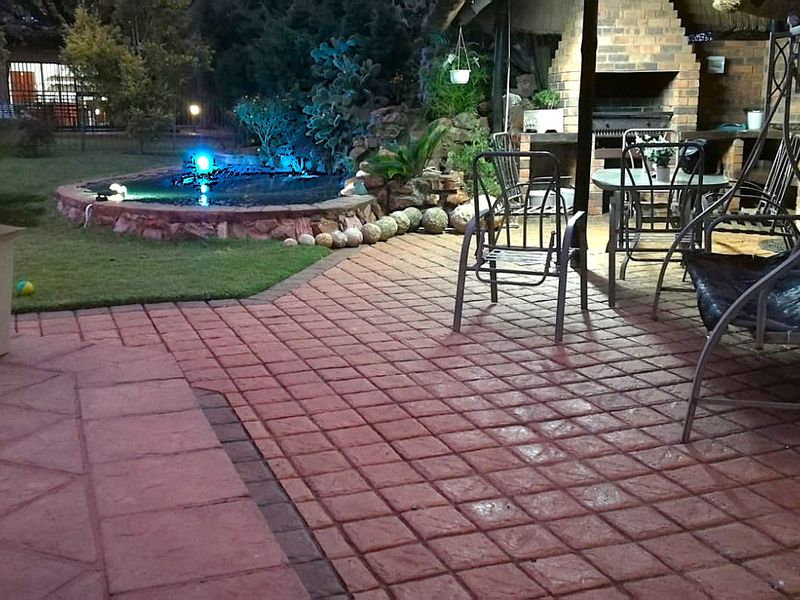 Covered outdoor patio featuring a built-in brick braai, paved flooring, and a landscaped stone-edged water feature in the garden.