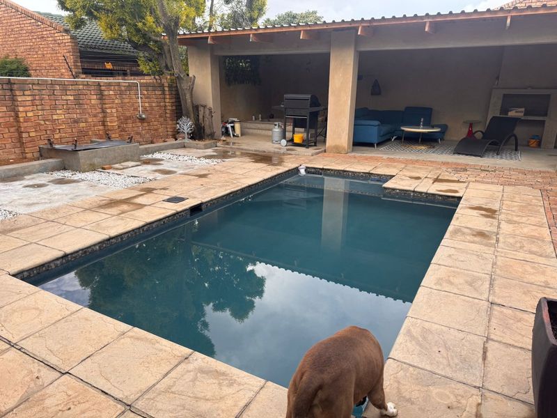 Outdoor entertainment area featuring a swimming pool, paved surround, and a covered patio with a built-in braai.