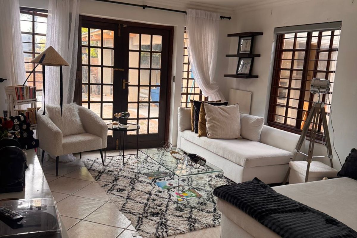 A bright living room featuring tiled flooring, a beadboard ceiling, and french doors leading to the exterior, complemented by large windows with security bars.