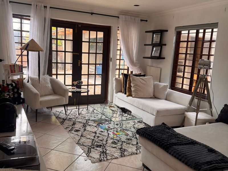 A bright living room featuring tiled flooring, a beadboard ceiling, and french doors leading to the exterior, complemented by large windows with security bars.