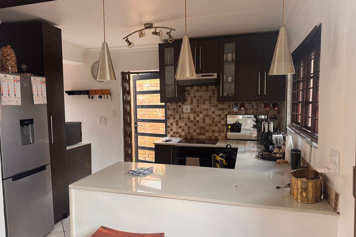 A functional kitchen featuring dark wood cabinetry, stone countertops, a mosaic tile backsplash, and integrated cooking appliances with direct access to the exterior.