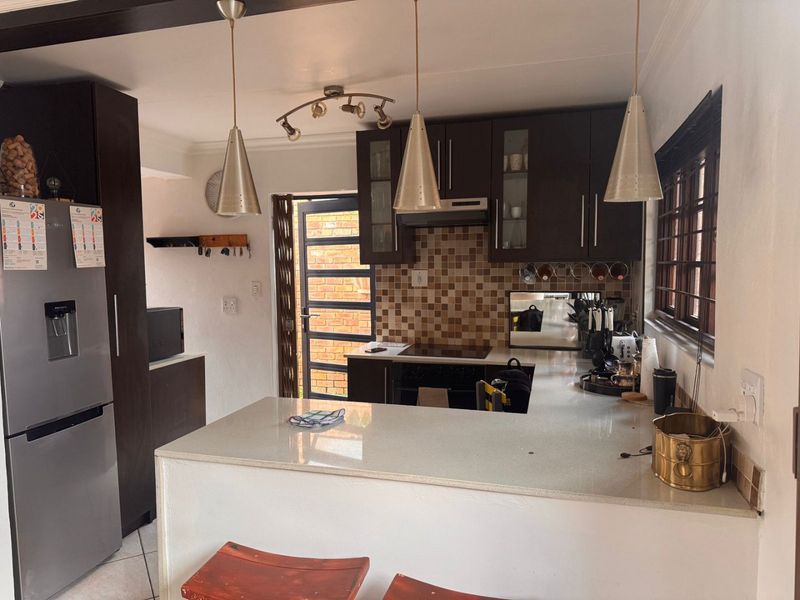 A functional kitchen featuring dark wood cabinetry, stone countertops, a mosaic tile backsplash, and integrated cooking appliances with direct access to the exterior.