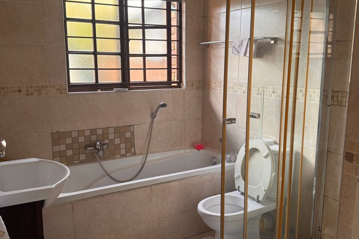 A functional bathroom featuring a bathtub, separate shower enclosure, pedestal basin, and toilet with neutral wall and floor tiling.