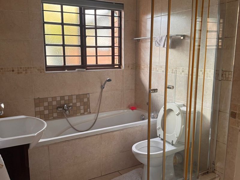 A functional bathroom featuring a bathtub, separate shower enclosure, pedestal basin, and toilet with neutral wall and floor tiling.