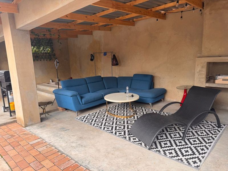 Covered outdoor patio area featuring exposed timber rafters, concrete flooring, and a built-in fireplace, providing a versatile space for outdoor living.