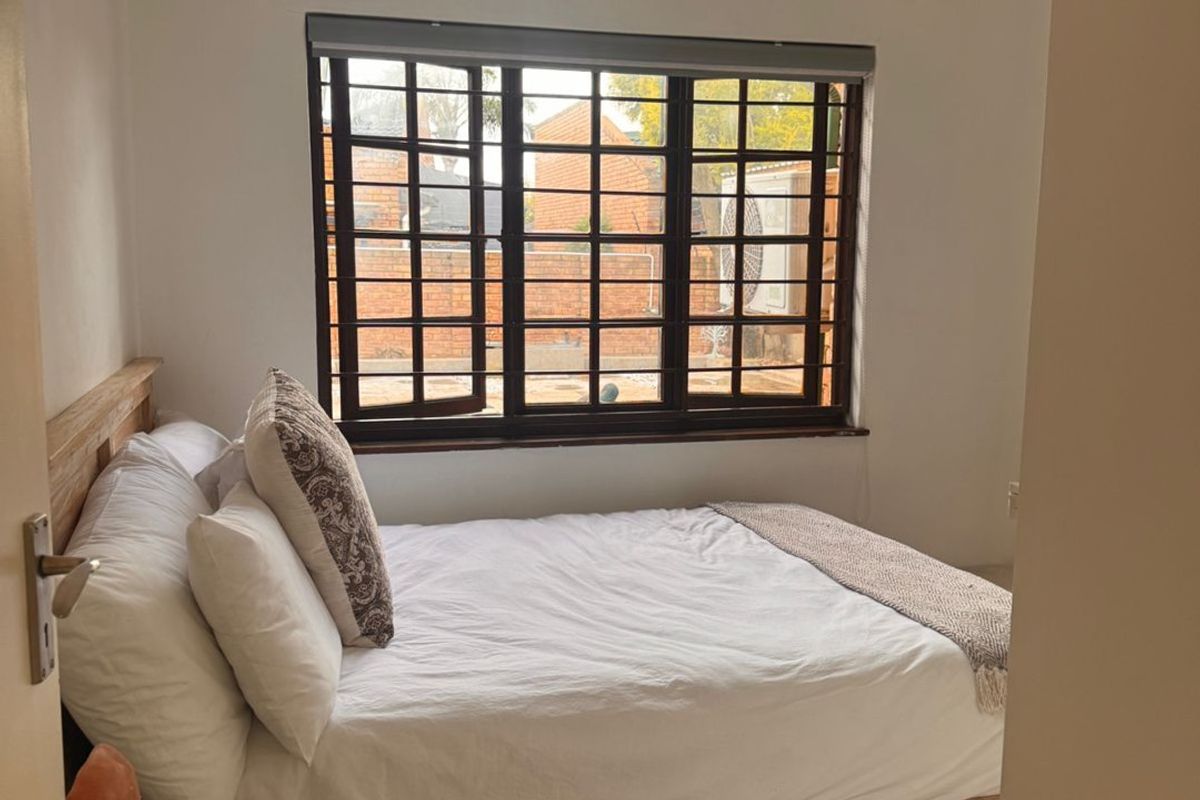 A cozy bedroom featuring a window with security bars, neutral walls, and a ceiling light fixture.