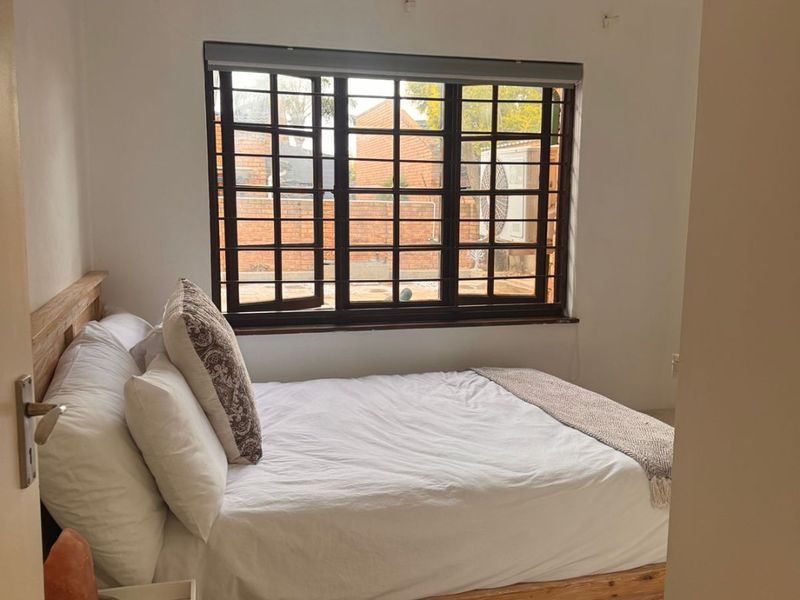 A cozy bedroom featuring a window with security bars, neutral walls, and a ceiling light fixture.