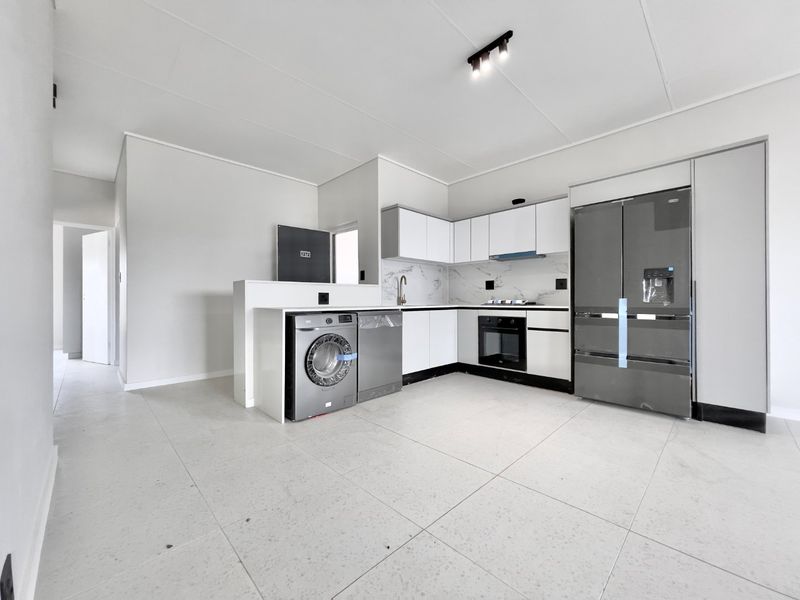 Modern, clean-lined kitchen featuring white cabinetry, marble-look backsplash, integrated appliances, and large format floor tiles in an open-plan layout.