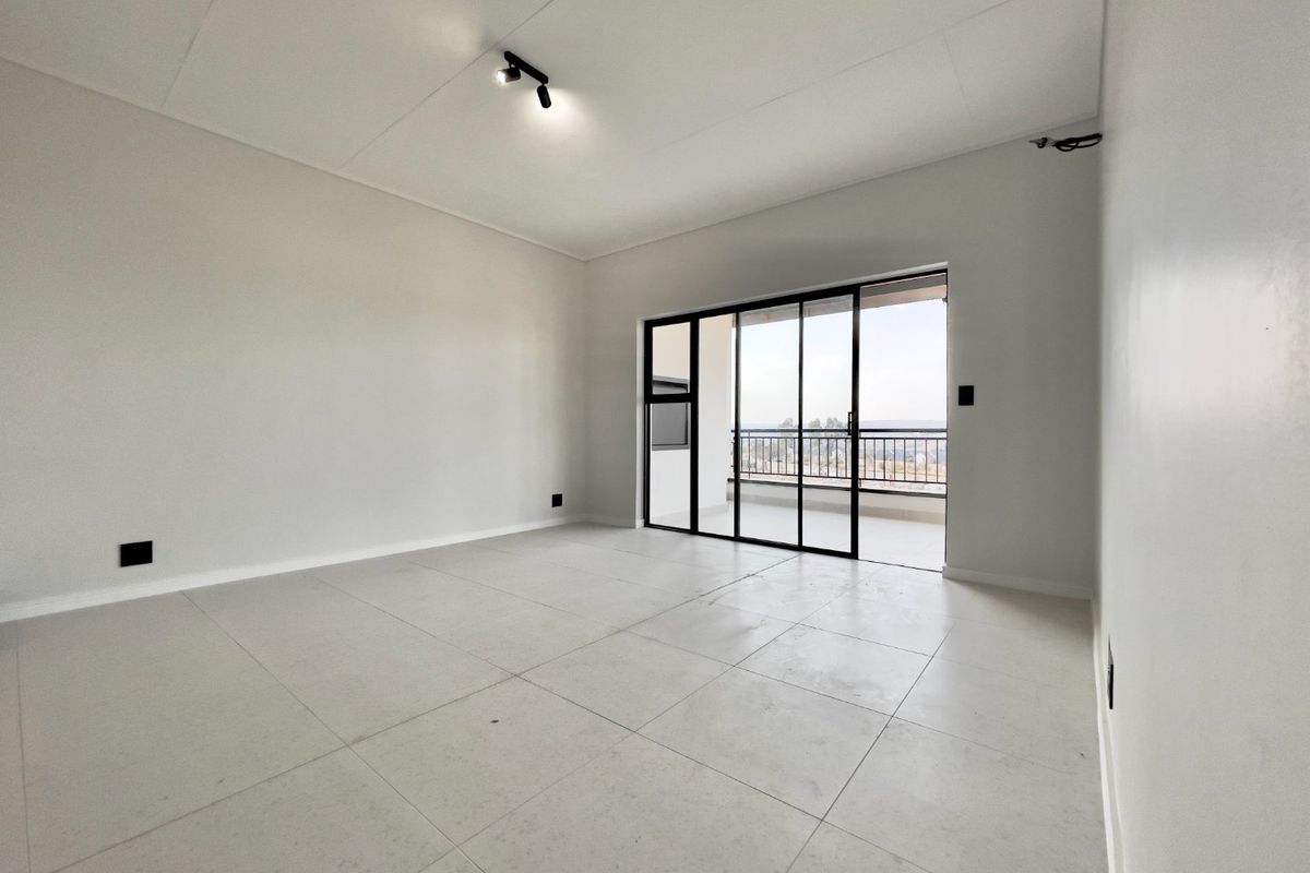 A bright, empty living area featuring neutral tiled flooring, modern track lighting, and large sliding glass doors leading to an outdoor balcony.