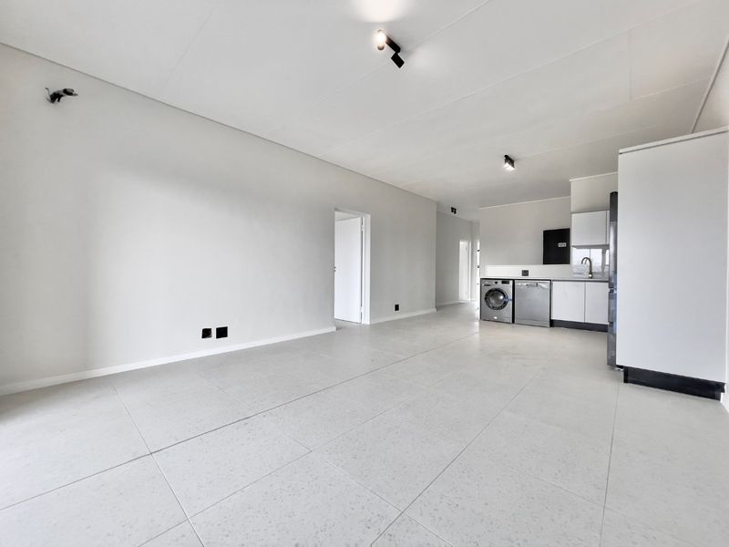 Spacious open-plan living area featuring modern tiled flooring, neutral walls, and a compact, functional kitchen with integrated appliances.