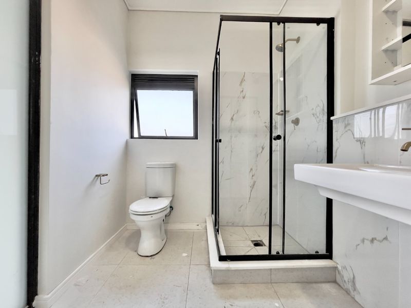 Modern bathroom featuring a glass-enclosed shower, wall-mounted basin, and elegant marble-look wall tiling with neutral floor tiles.