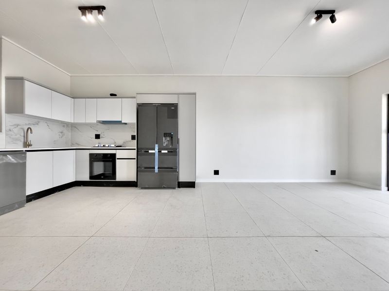 Modern open-plan kitchen featuring sleek white cabinetry, marble-look splashbacks, integrated appliances, and large format floor tiles in a bright, minimalist space.