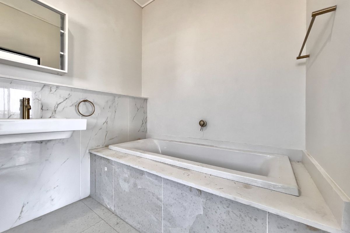 Modern bathroom featuring a built-in bathtub, wall-mounted basin, marble-look tiling, and brass-finish fixtures in a clean, minimalist setting.