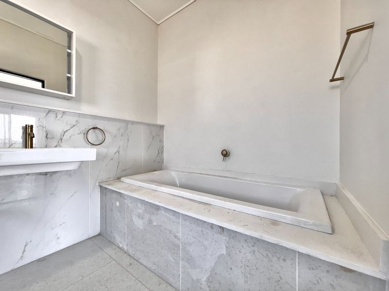 Modern bathroom featuring a built-in bathtub, wall-mounted basin, marble-look tiling, and brass-finish fixtures in a clean, minimalist setting.