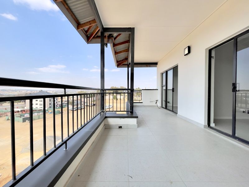 A spacious, modern covered balcony featuring tiled flooring, a sleek metal balustrade, and large sliding glass doors providing access to the interior.