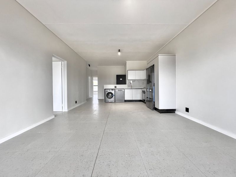 Spacious open-plan living area featuring a modern kitchen with built-in cabinetry, integrated appliances, and neutral tiled flooring throughout.