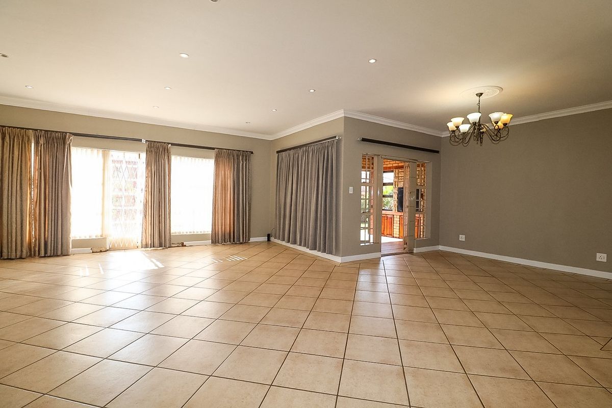 Spacious, open-plan living area featuring neutral tiled flooring, recessed downlighting, decorative chandelier, and large sliding glass doors providing access to the exterior.