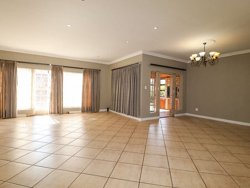Spacious, open-plan living area featuring neutral tiled flooring, recessed downlighting, decorative chandelier, and large sliding glass doors providing access to the exterior.