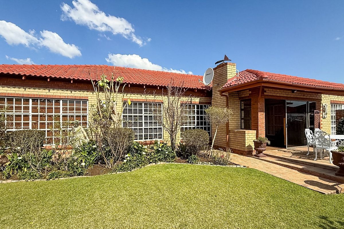 Rear view of the townhouse featuring a brick facade, tiled roof, paved patio area, and well-maintained garden space.