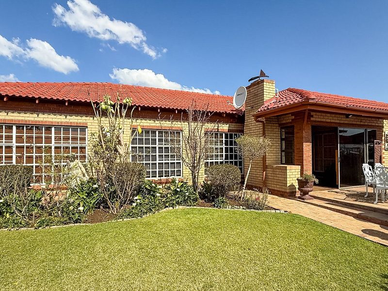Rear view of the townhouse featuring a brick facade, tiled roof, paved patio area, and well-maintained garden space.