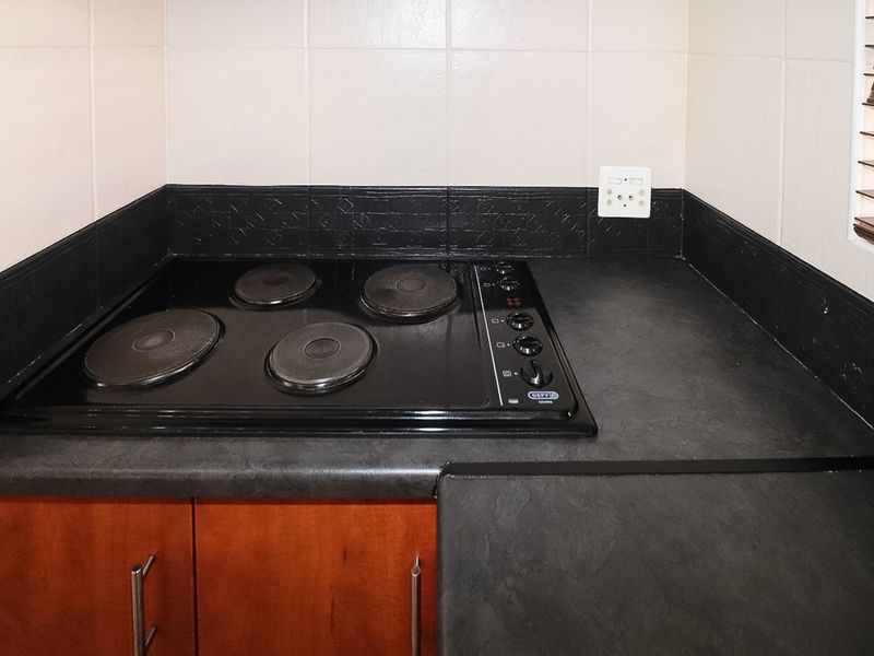A close-up view of a kitchen workspace featuring a built-in electric hob, dark laminate countertops, and wooden cabinetry with tiled splashbacks.