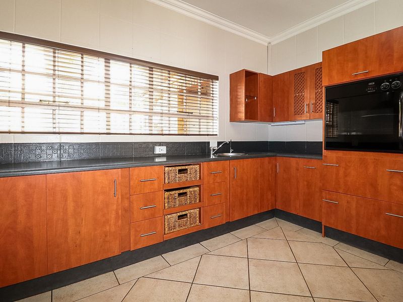 A functional kitchen featuring wood-finish cabinetry, dark countertops, built-in oven, and tiled flooring, offering a clean and practical workspace.