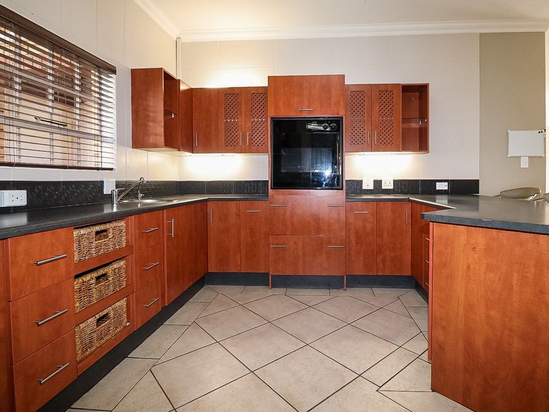 A functional kitchen featuring warm-toned cabinetry, dark countertops, built-in oven, and tiled flooring, offering a practical layout for daily meal preparation.