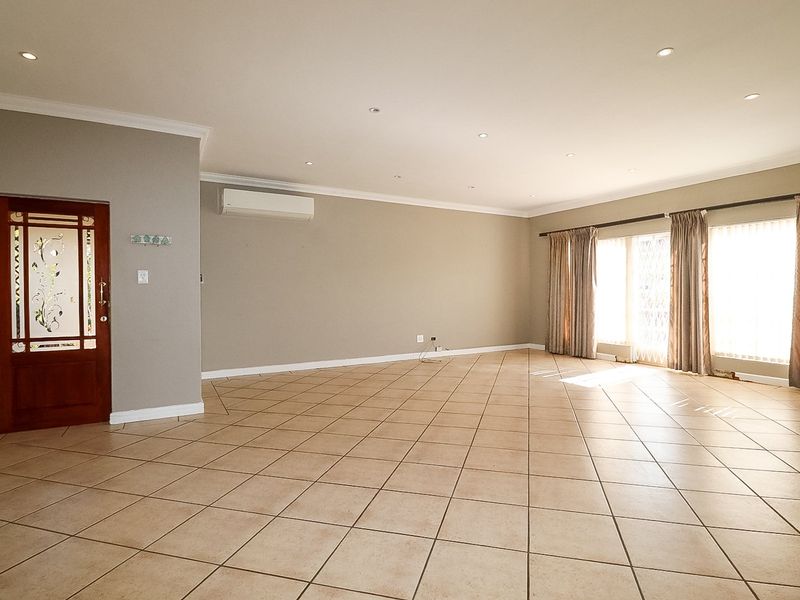 Spacious, light-filled living area featuring neutral-toned ceramic floor tiles, recessed downlighting, and a wall-mounted air conditioning unit.