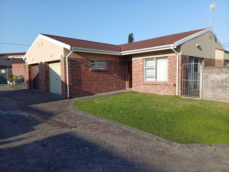 Front elevation of a single-story townhouse featuring a brick facade, tiled roof, double garage, and a paved driveway with a small front lawn.