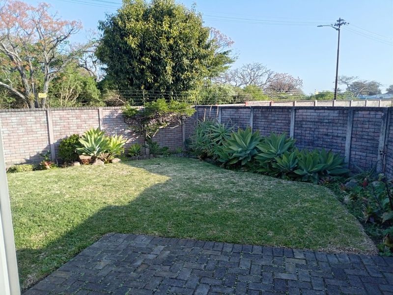 A private rear garden featuring a well-maintained lawn, paved patio area, and secure brick boundary walls with electric fencing.