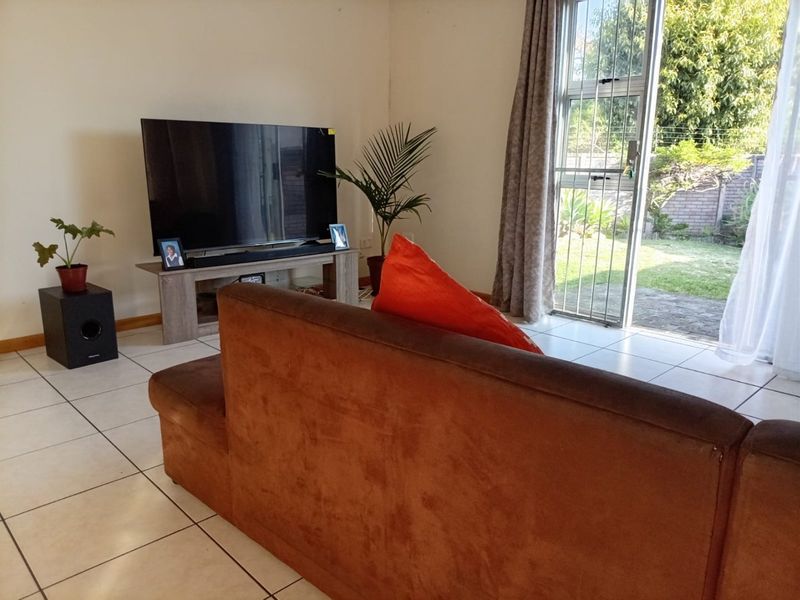 A living room featuring light-colored floor tiles and a sliding glass door with a security gate providing access to the garden.