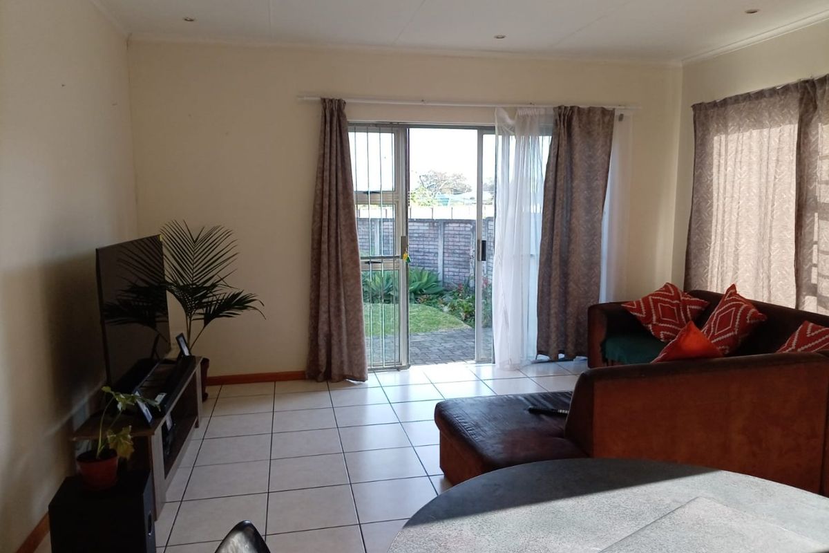 A living room featuring tiled flooring and a sliding glass door with a security gate, providing direct access to the rear garden area.