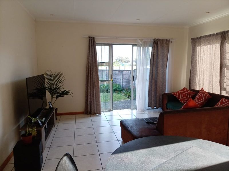 A living room featuring tiled flooring and a sliding glass door with a security gate, providing direct access to the rear garden area.