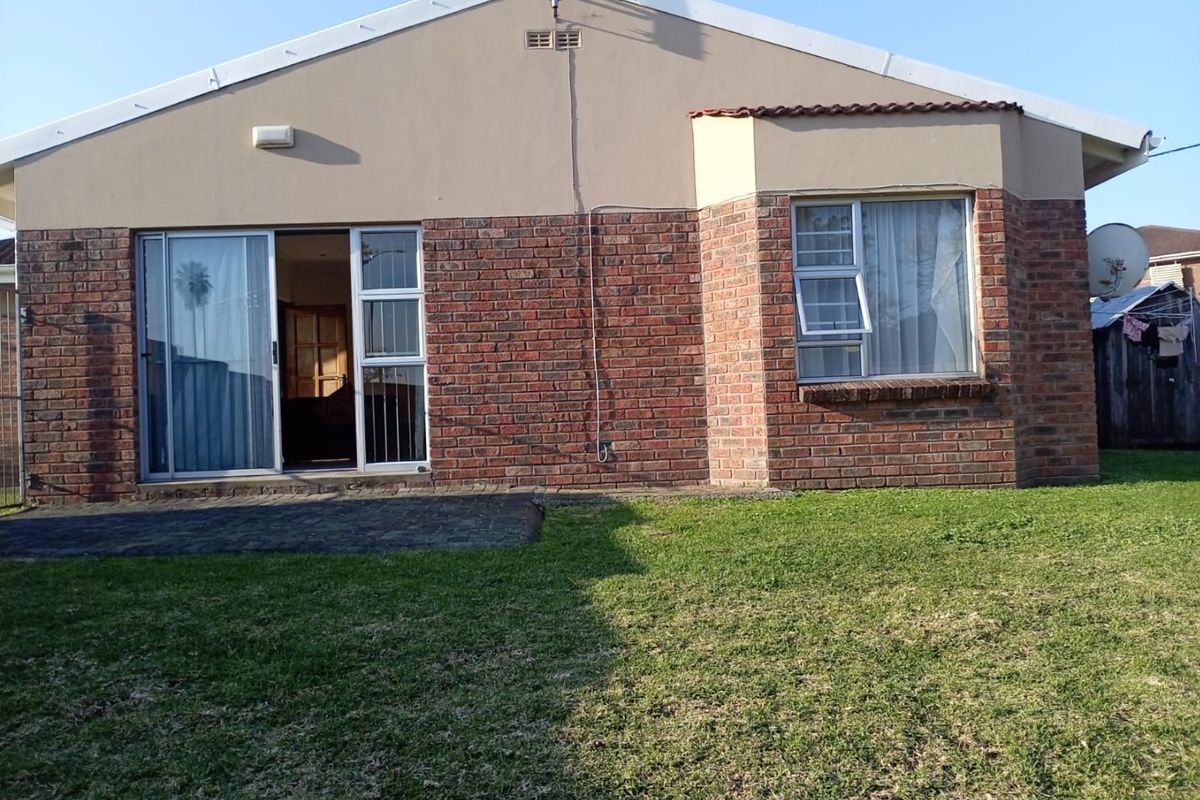 Rear view of the townhouse featuring a brick facade, paved patio area, and a small private lawn.