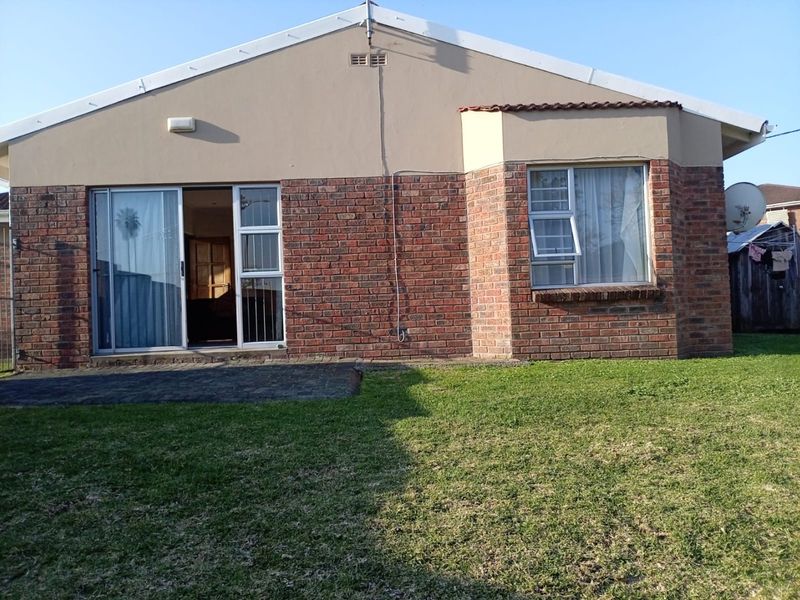 Rear view of the townhouse featuring a brick facade, paved patio area, and a small private lawn.
