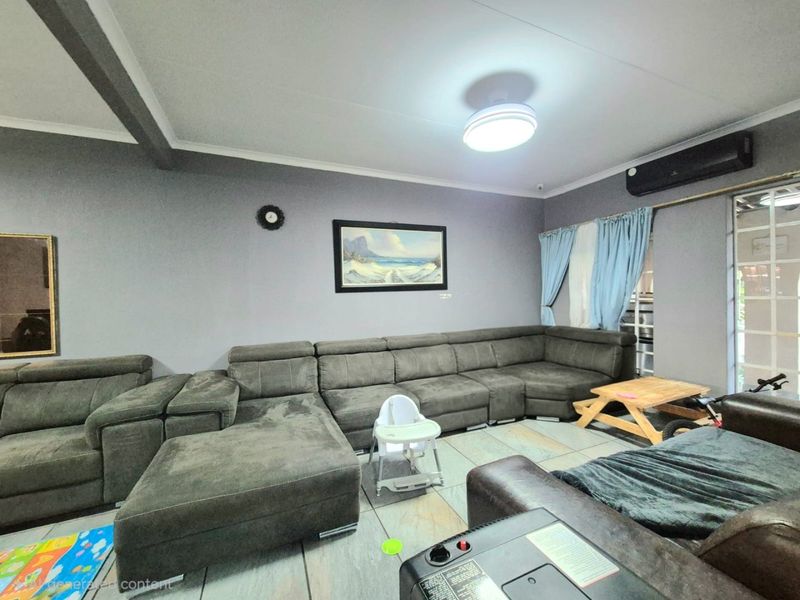 A living room featuring tiled flooring, a wall-mounted air conditioning unit, and a sliding door leading to the exterior.