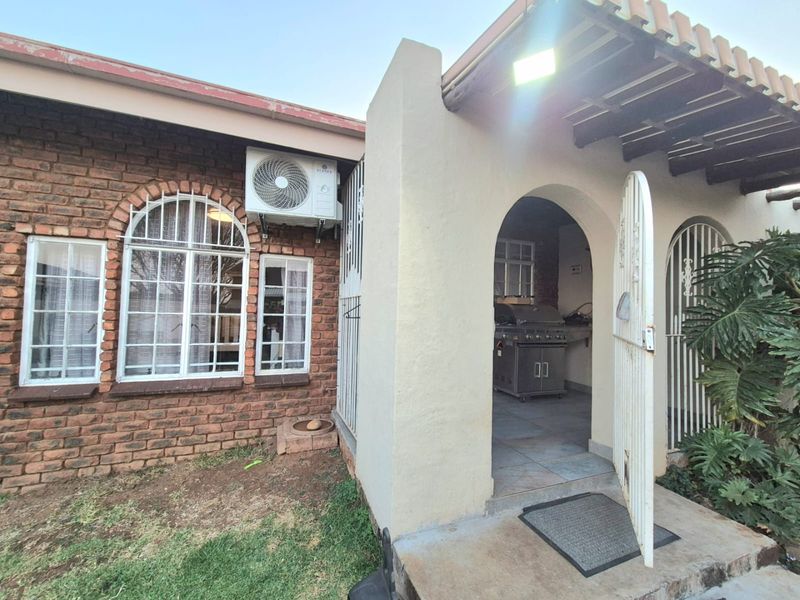 Covered patio area featuring a built-in braai, tiled flooring, and direct access to the garden through an arched entrance.