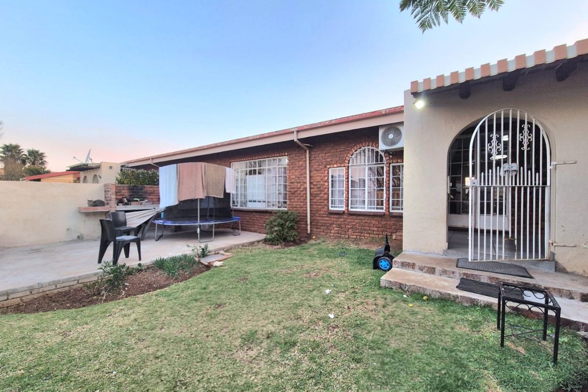 Rear exterior view of the townhouse featuring a brick facade, a paved patio area with a built-in braai, and a small garden space.