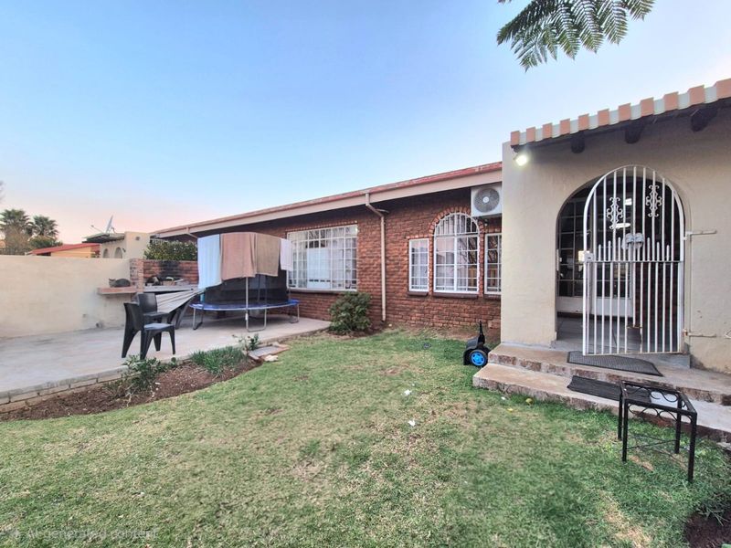Rear exterior view of the townhouse featuring a brick facade, a paved patio area with a built-in braai, and a small garden space.