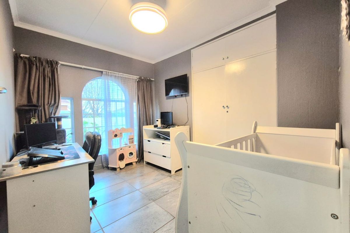 A bedroom featuring tiled flooring, built-in cupboards, and a distinctive arched window, providing a functional space with neutral wall tones.