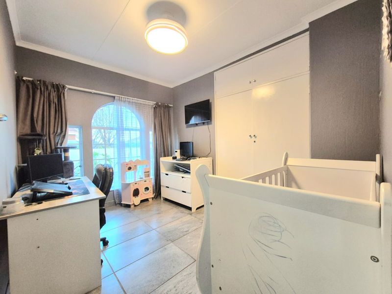 A bedroom featuring tiled flooring, built-in cupboards, and a distinctive arched window, providing a functional space with neutral wall tones.