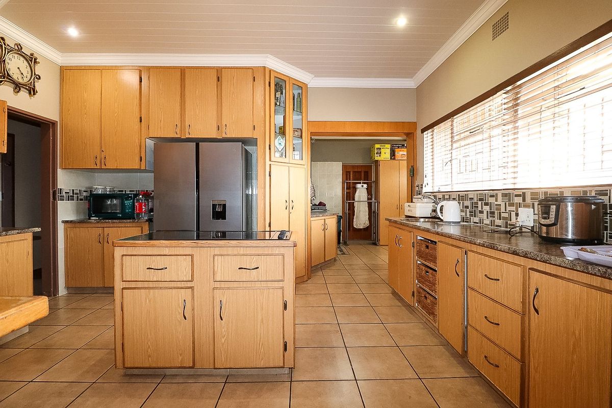 Spacious kitchen featuring extensive timber cabinetry, a central island, tiled flooring, and a mosaic tile backsplash with ample counter space.