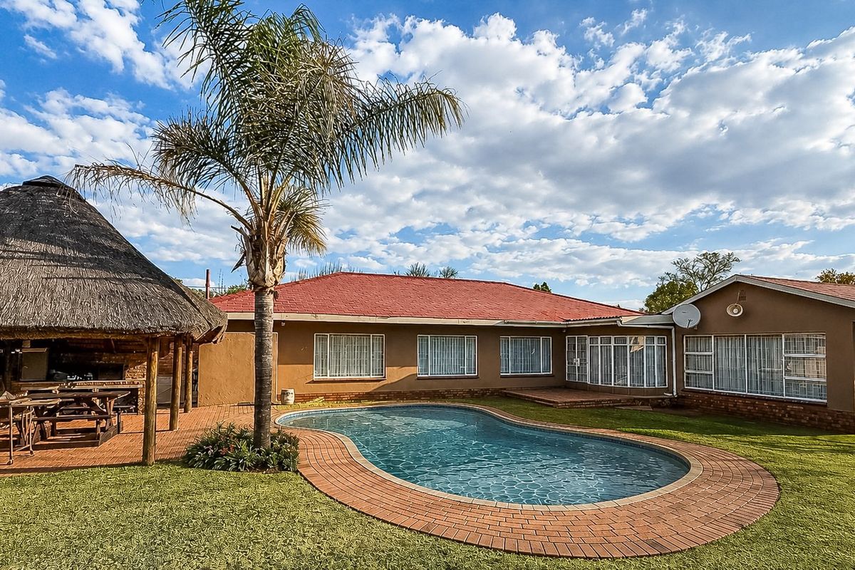 Rear exterior view featuring a swimming pool, brick-paved surround, and a spacious thatched lapa with a built-in braai area.