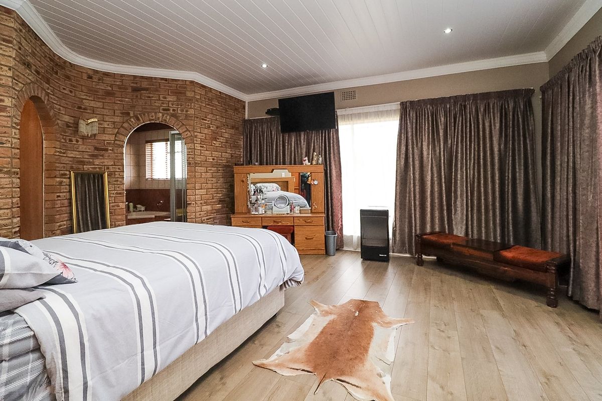 Spacious bedroom featuring exposed brick feature walls, laminate flooring, recessed lighting, and an arched entryway leading to an en-suite bathroom.